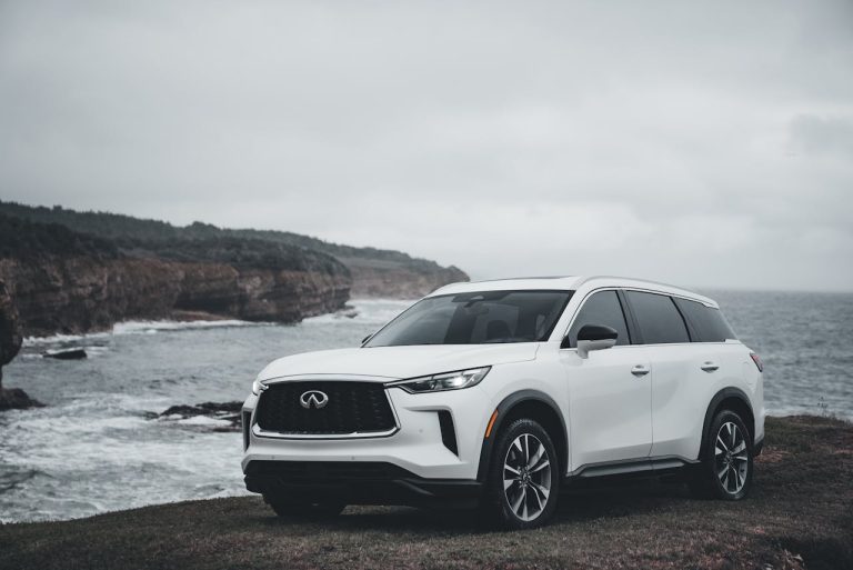 White SUV parked by a rugged coastal landscape with ocean view.